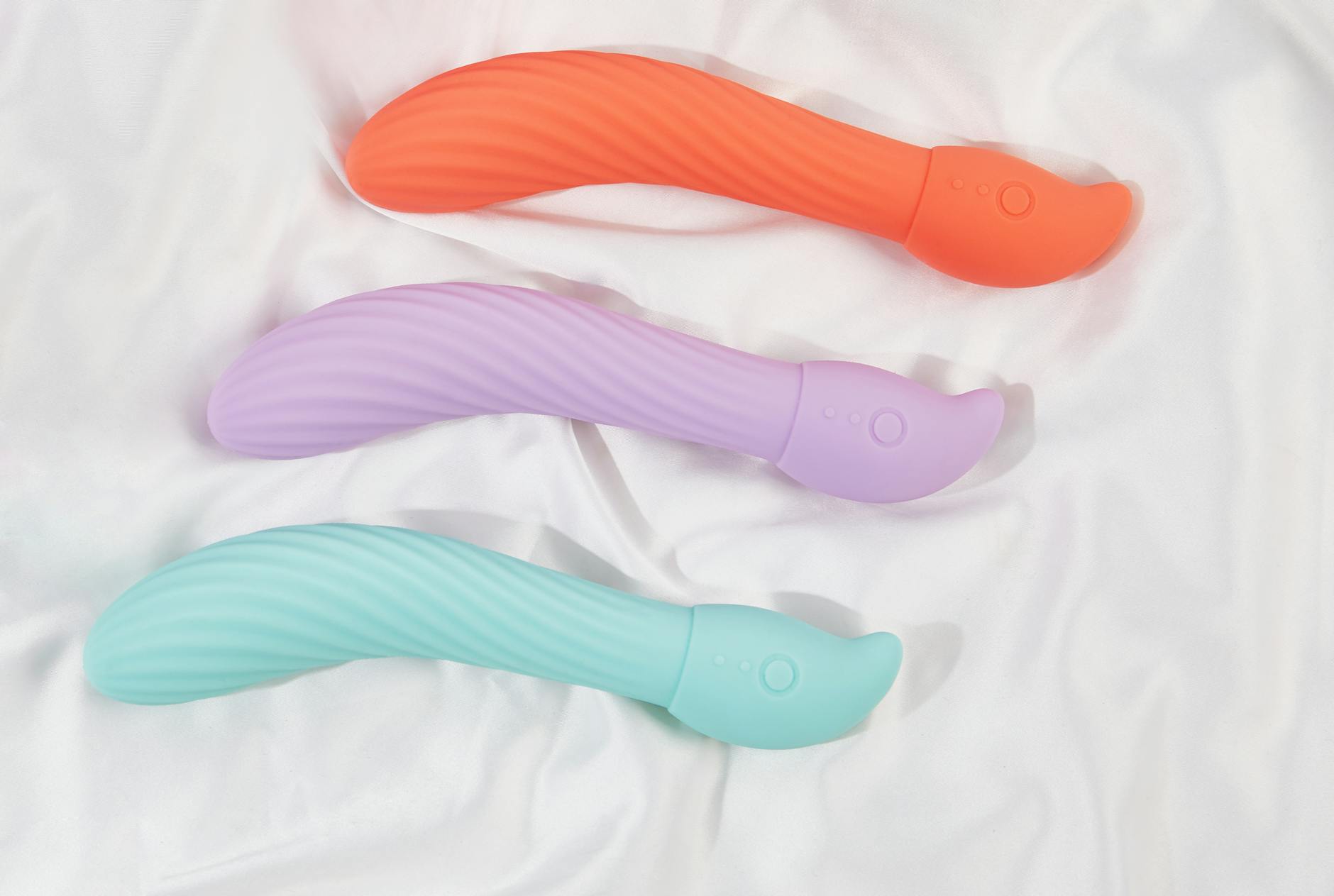 Three colorful silicone vibrators arranged on white fabric