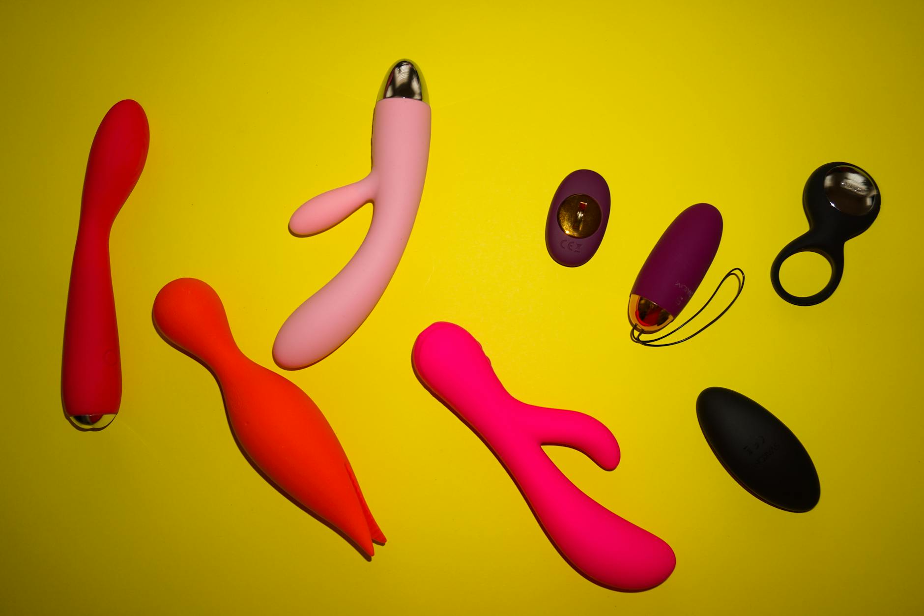 Diferentes brinquedos sexuais coloridos exibidos em superfície amarela vibrante