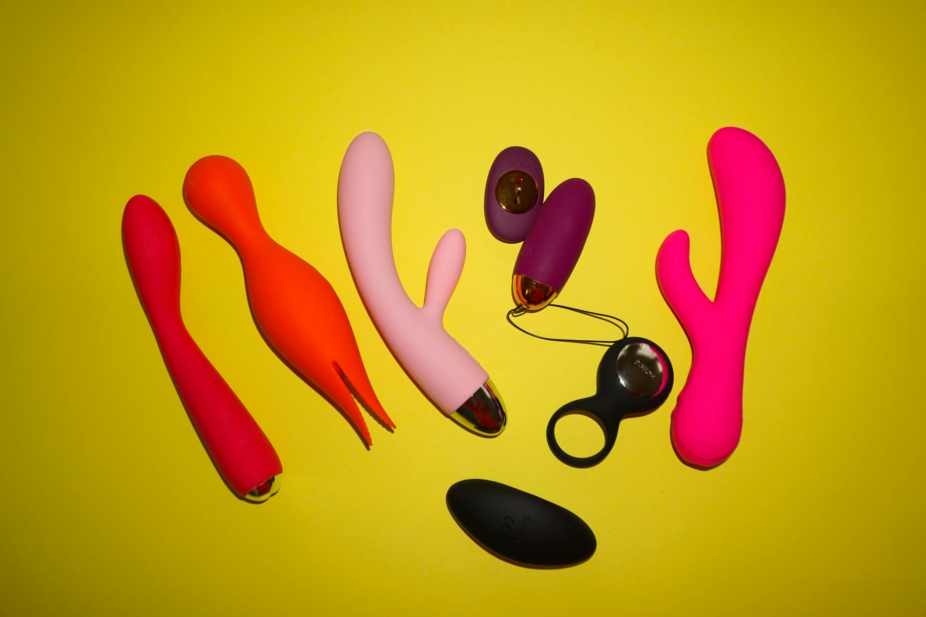 Vibrador azul rodeado por flores e fatias de laranja em fundo amarelo vibrante