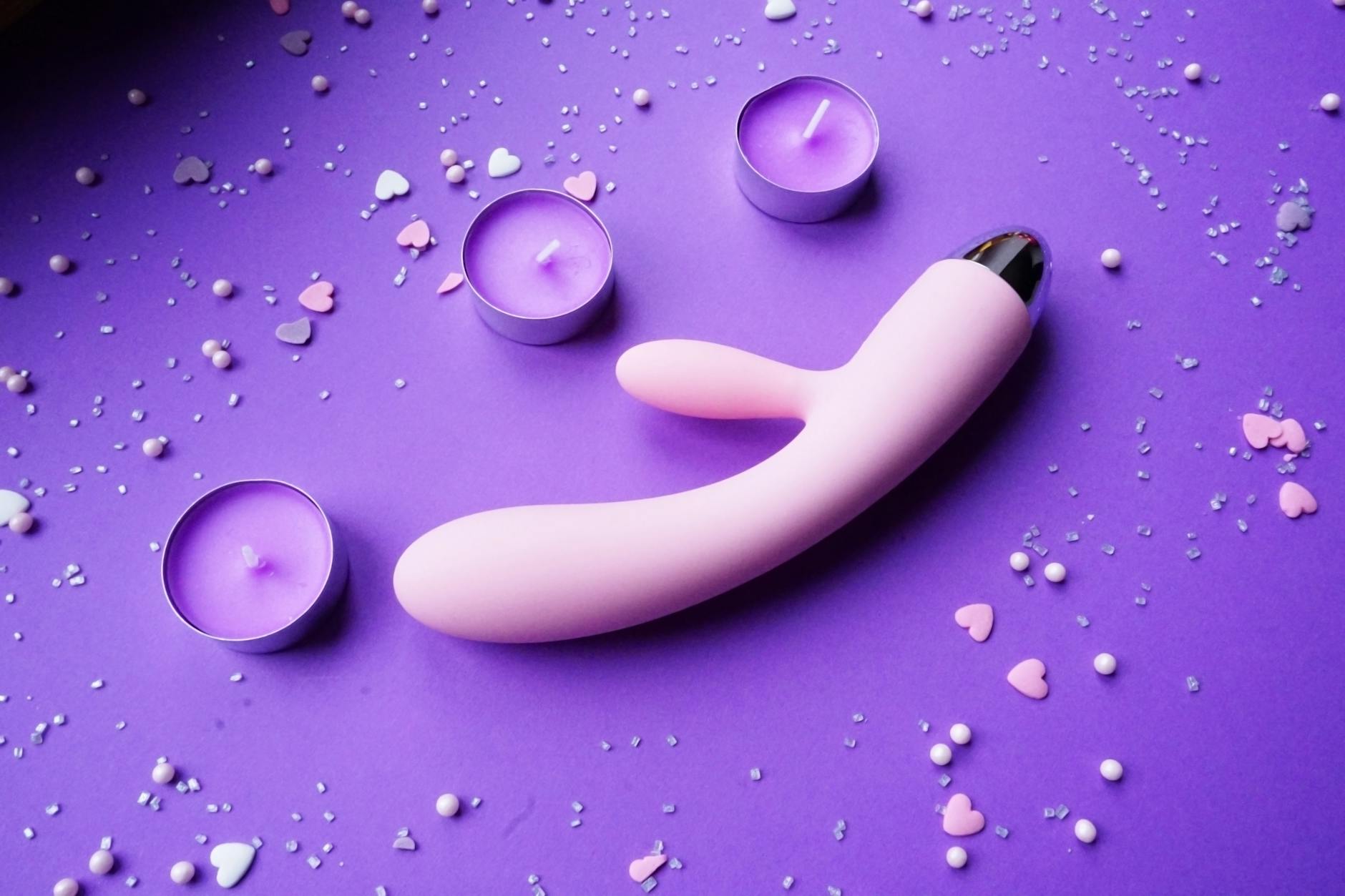 Pink vibrator on a purple background with heart confetti and candles for a romantic vibe